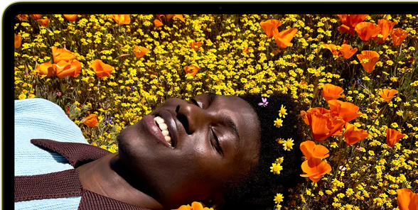 MacBook Neo, kleur Citrus, op het scherm een lachende persoon die in een zonnig bloemenveld ligt
